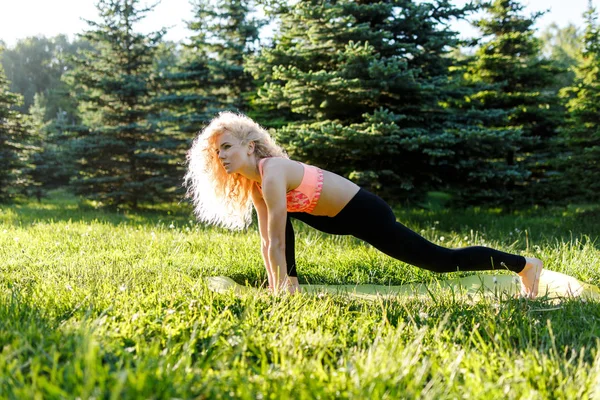 Beeld van jonge curly-haired sport vrouw beoefenen van yoga op tapijt in park — Stockfoto