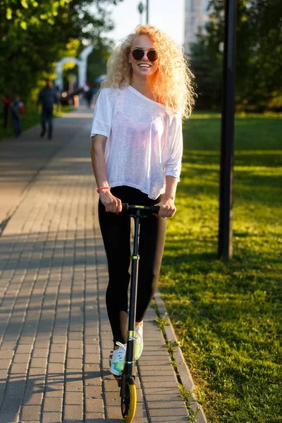 Zdjęcie z kręconych włosach kobiety lekkoatletycznego jazda skuterem w parku — Zdjęcie stockowe