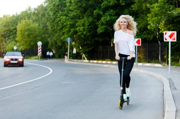 Tam uzunlukta Park scooter üzerinde tekme kıvırcık saçlı atletik kadın fotoğrafı — Stok fotoğraf