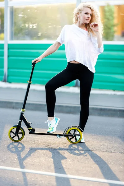 Foto completa de mulher atlética de cabelos encaracolados chutando em scooter no parque — Fotografia de Stock