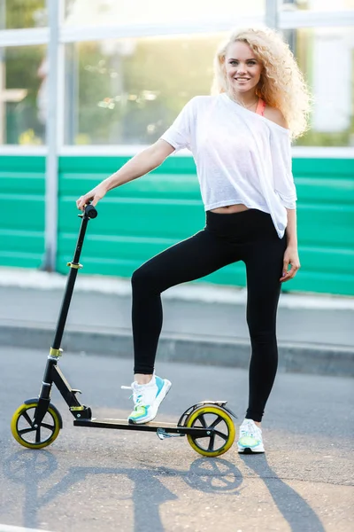 Foto completa de mulher atlética de cabelos encaracolados chutando em scooter no parque — Fotografia de Stock