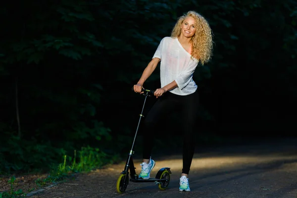 Imagem completa de mulher atlética de cabelos encaracolados chutando em scooter no parque — Fotografia de Stock