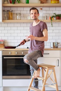 Kızartma tavası ve mutfakta elinde telefon ile brunet adam resmi