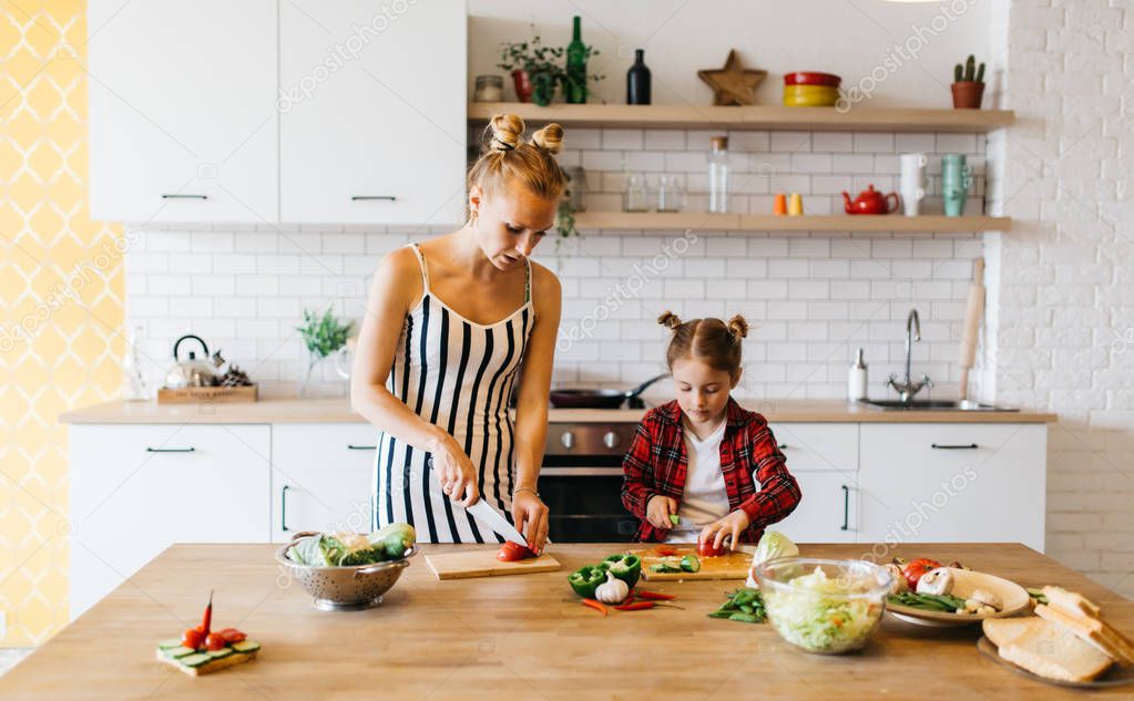 Photo of beautiful woman with her daughter cutting vegetables in kitchen