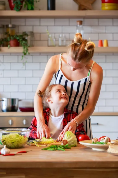 Foto mladé matky s její dcerou krájení zeleniny v kuchyni — Stock fotografie
