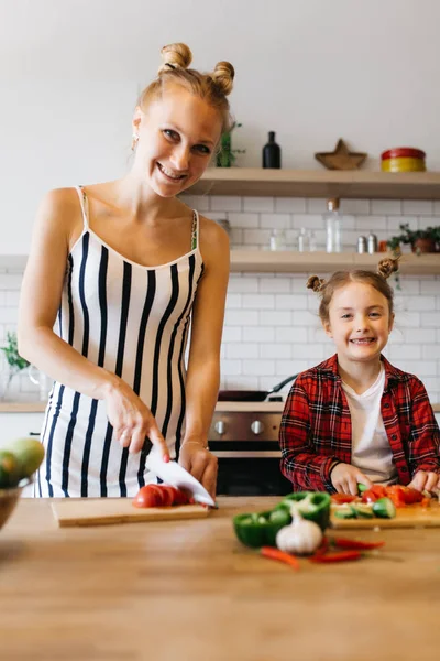Foto krásné ženy s její dcerou krájení zeleniny v kuchyni — Stock fotografie