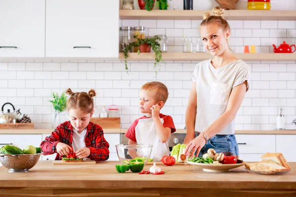 Foto krásné matky s dcerou a synem krájení zeleniny u stolu — Stock fotografie