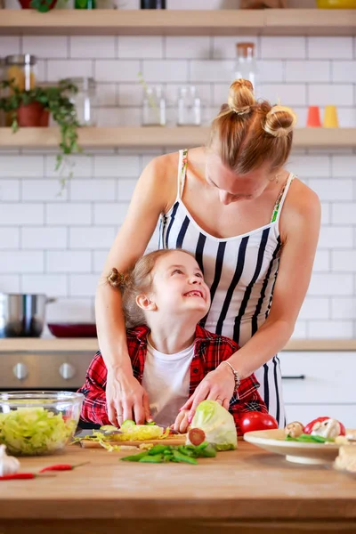Snímek mladé matky s její dcerou krájení zeleniny v kuchyni — Stock fotografie