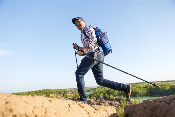 Bild eines jungen Touristenmannes mit Wanderstöcken, der in bergiger Gegend unterwegs ist — Stockfoto