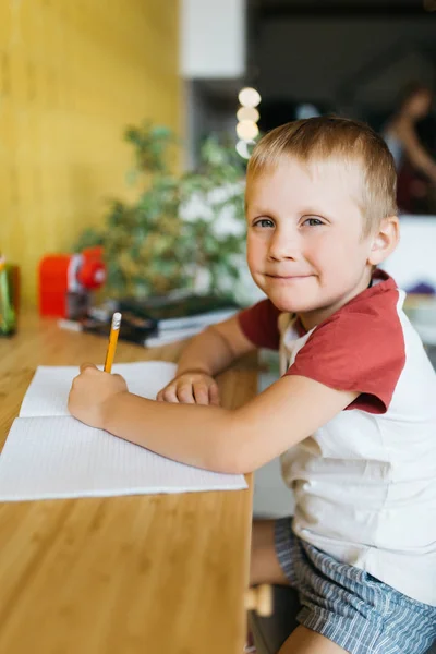 Фото хлопчика з ручкою і блокнотом, що сидить за столом — стокове фото