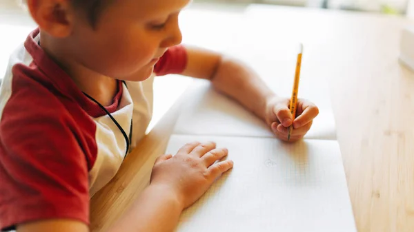 Imagem do menino com caneta e caderno sentado à mesa — Fotografia de Stock