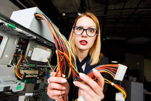 Photo of woman with glasses holding wire in hands at table next to broken processor — Stock Photo, Image