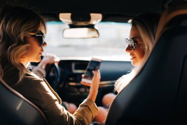 Arabanın içinde otururken elinde telefon ile uzun saçlı iki konuşan kadın arka fotoğraf