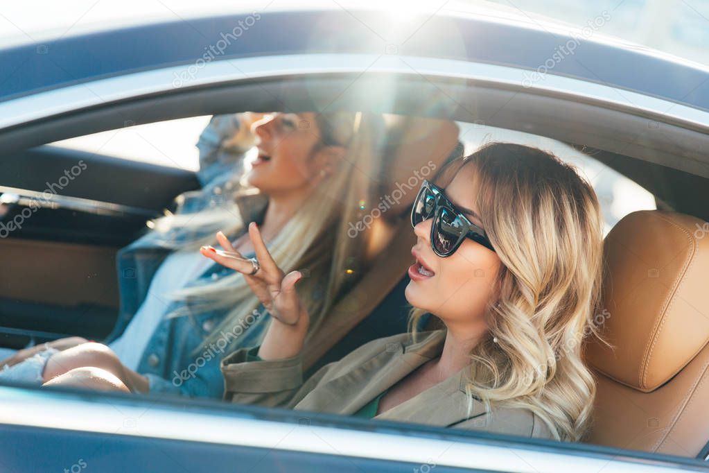 Photo of side of blondes wearing sunglasses while driving in car