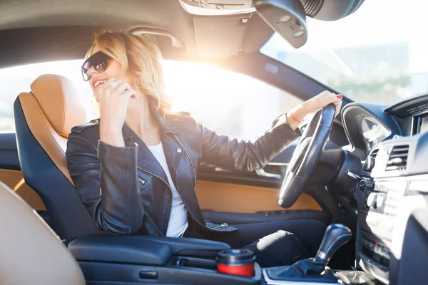 Foto di lato della bionda in occhiali neri seduto dietro la ruota in auto — Foto Stock