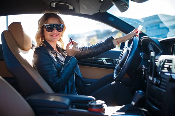 Foto de rubia feliz en gafas negras pinta los labios sentados en el coche —  Fotos de Stock