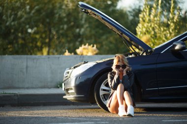 Açık hood ile kırık arabanın yakınında oturan genç kadın fotoğrafı