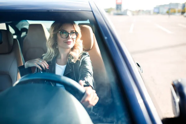 Изображение молодой женщины в очках за рулем черной машины — стоковое фото