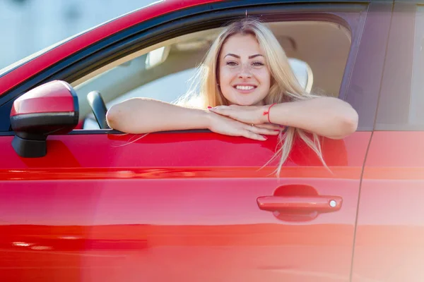 Foto de mujer rubia feliz sentada en coche rojo con ventana abierta —  Fotos de Stock