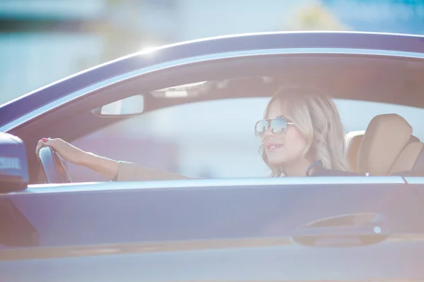 Foto de hermosa rubia en gafas de sol sentada en coche negro —  Fotos de Stock