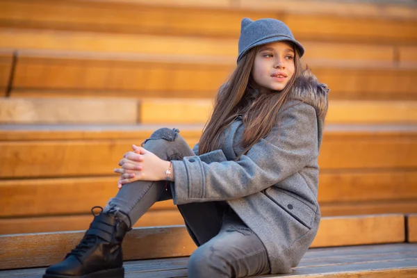 Foto de chica de abrigo gris sentada en un banco de madera —  Fotos de Stock