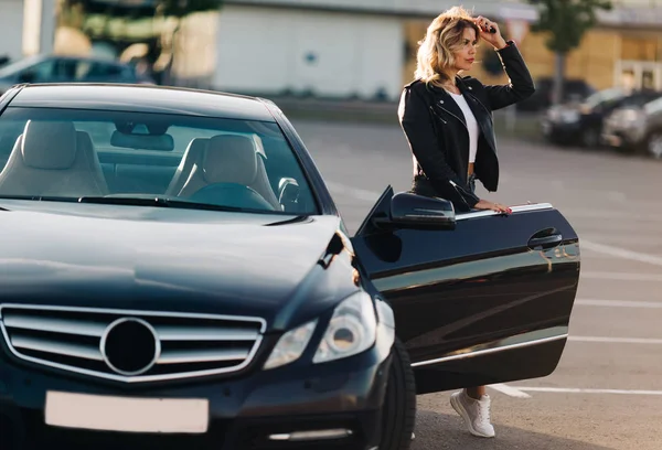 Фото симпатичной блондинки у открытой двери черного автомобиля — стоковое фото