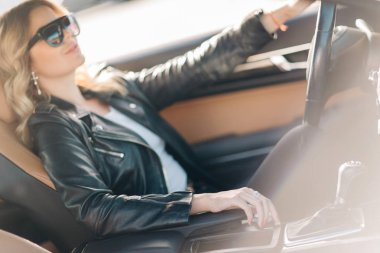 Görüntü siyah gözlüklü siyah arabada oturan kıvırcık saçlı uzun saçlı sarışın.