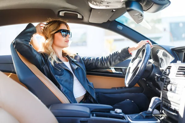 Foto di lato della donna bionda in occhiali neri seduto dietro la ruota in auto — Foto Stock