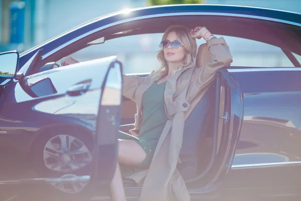 Фото девушки в очках и длинном платье, сидящей в машине с открытой дверью — стоковое фото