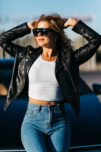 Retrato de jovem loira em óculos de sol de pé ao lado do carro preto — Fotografia de Stock