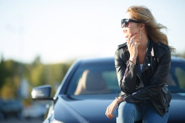 Görüntü siyah araba kaputa oturan güneş gözlüklü genç kadın