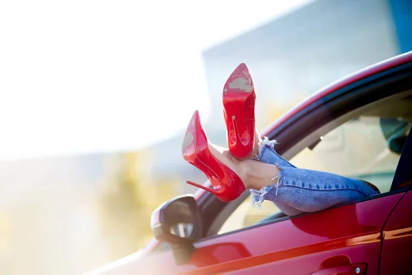 Foto de pernas de mulher em sapatos vermelhos saindo da janela do carro vermelho — Fotografia de Stock