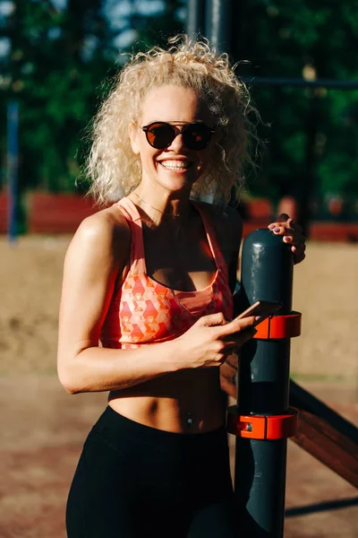 Foto av sport kvinna bär solglasögon håller telefonen i händer — Stockfoto