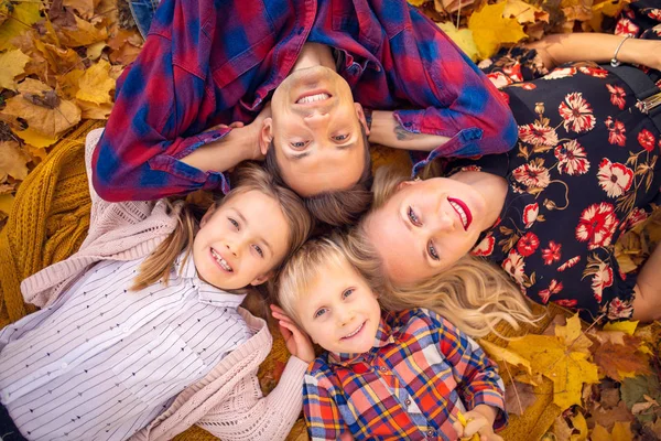 Foto von oben von liegenden Eltern mit Kindern auf gelben Blättern im Park — Stockfoto