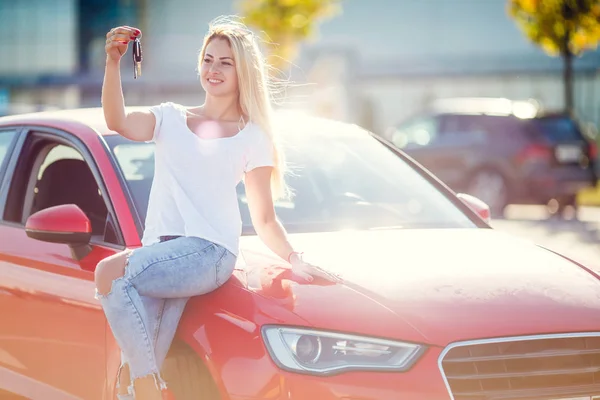 Фото счастливой блондинки с ключами, стоящими возле красного автомобиля в летний день . — стоковое фото