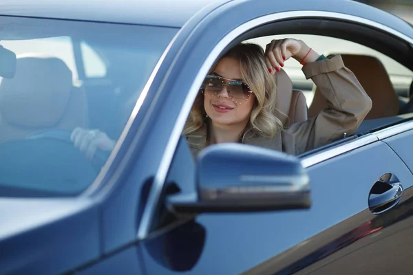Foto de la joven rubia en gafas de sol sentada en coche negro —  Fotos de Stock