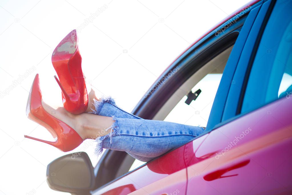 Image of womans legs in red shoes sticking out of red car window