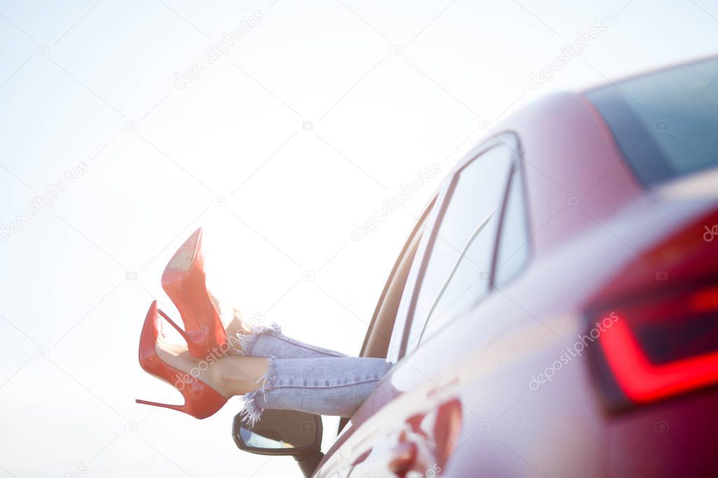 Photo of girls legs in red shoes sticking out of red car window