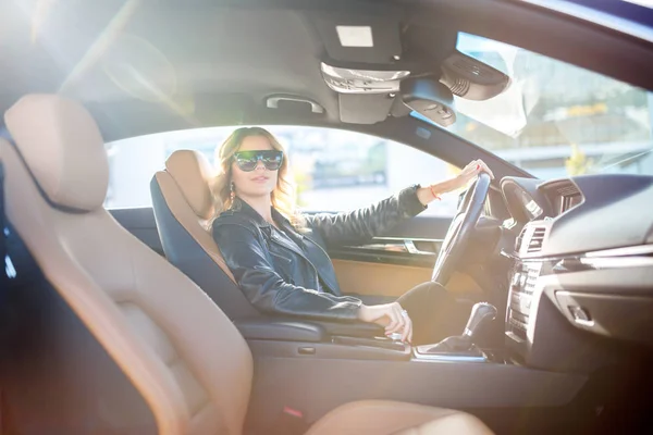 Immagine di lato della bionda in occhiali neri seduta dietro la ruota in auto — Foto Stock