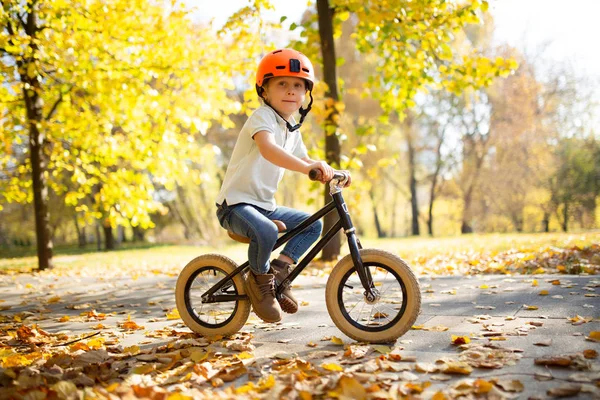 Foto do menino em capacete vermelho em bicicleta de corrida no parque de outono — Fotografia de Stock