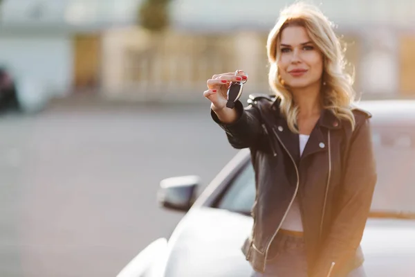 Изображение молодой блондинки с ключами на капоте черной машины — стоковое фото