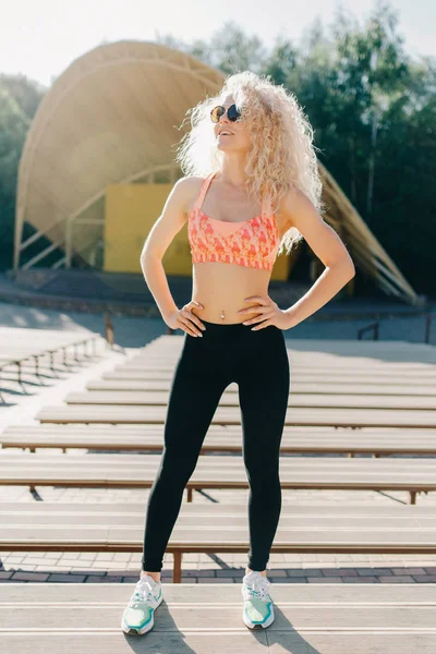 Foto van curly-haired atletische vrouw permanent in park onder winkel — Stockfoto