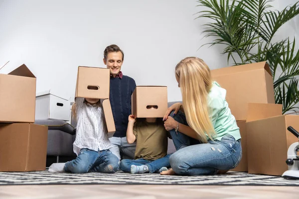 Kép a szülők és a gyermekek karton dobozok a fejükre, új lakás — Stock Fotó