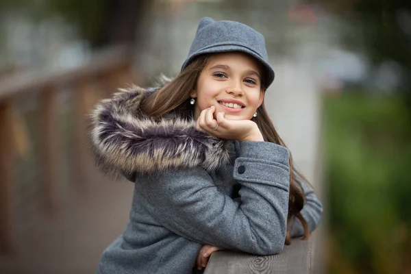 Фото девушки в серой шляпе и пальто на деревянном мосту в городе — стоковое фото