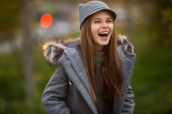 灰色の帽子や都市で背景をぼかした写真のコートの女の子の写真 — ストック写真