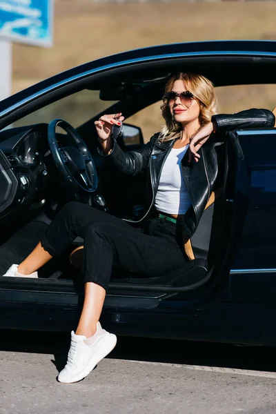 Изображение молодой блондинки с ключами, сидящей в машине с открытой дверью — стоковое фото
