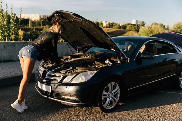 Foto no lado da mulher em pé na frente do carro preto com capuz aberto — Fotografia de Stock