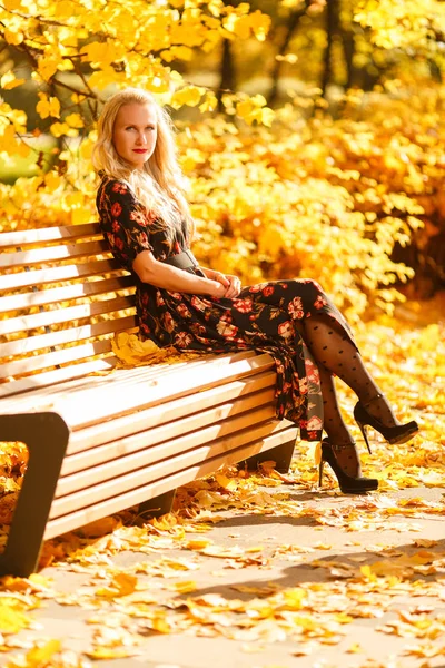 Foto de loira sentada no banco de madeira no parque de outono — Fotografia de Stock