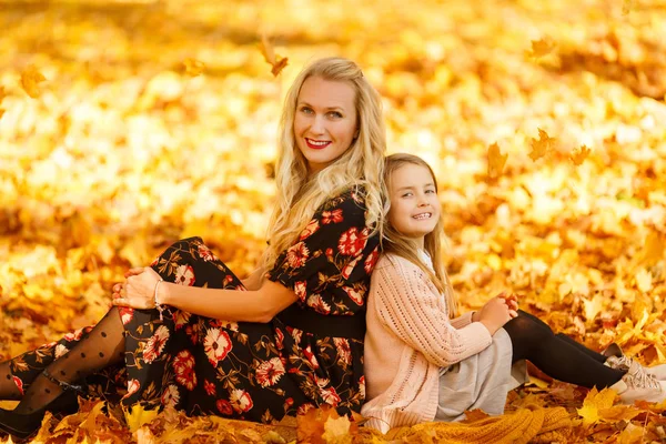 Photo of mother and daughter sitting on leaves in autumn — Stock Photo, Image