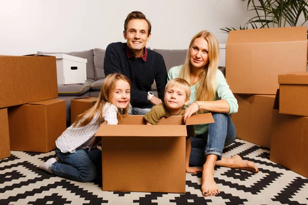 Фото счастливых родителей с детьми, сидящими на полу среди картонных коробок — стоковое фото